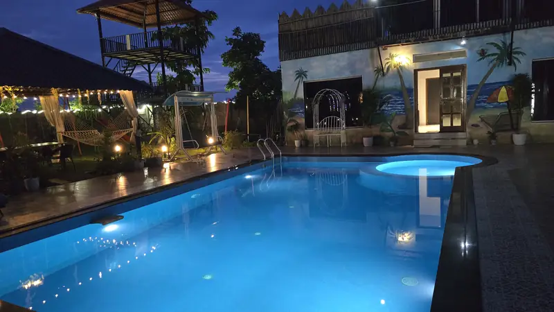 The pool glowing blue at dusk, with the hall and machan lit behind