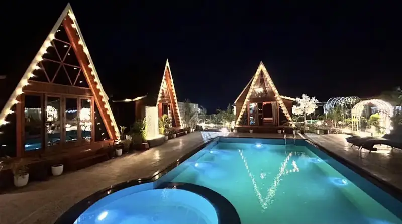Three lit A-frames around the pool at night
